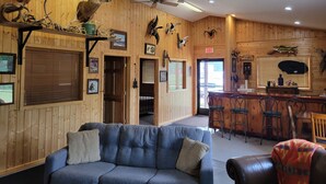 Quarto com decoração em madeira, um sofá azul, um espaço de bar com banquetas e diversas cabeças de animais montadas nas paredes.