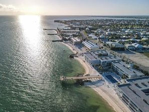 An aerial view of a coastal town with a beachfront hotel, a pier, and a marina.