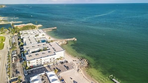 Vista aérea de un hotel costero con estacionamiento, acceso a la playa y un muelle que se adentra en el agua.