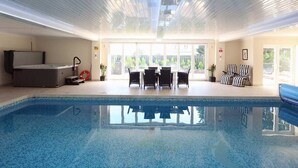 An indoor swimming pool with a clear view of the outdoors, a seating area with chairs, and a small table. - Torbay Rise Seaside Villa with outstanding family facilities (Torquay)