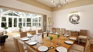 A spacious dining area with a long wooden table set for a meal, surrounded by wicker chairs. - Torbay Rise Seaside Villa with outstanding family facilities (Torquay)
