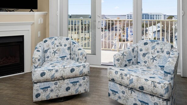 Two upholstered chairs with a nautical theme, a fireplace, and a large window with a view of buildings and a road. - Adagio - side unit in ofront bldg, 3br/3bath indoor pool (Ocean City)