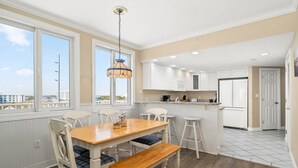 A modern kitchen with white cabinetry, a wooden dining table with blue cushions, and a hanging pendant light. - Adagio - side unit in ofront bldg, 3br/3bath indoor pool (Ocean City)