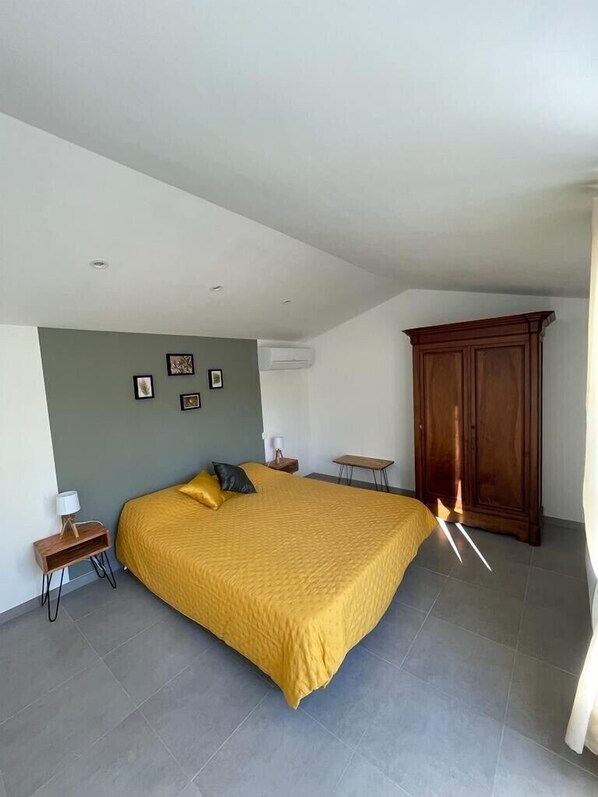 A bedroom with a large bed, a wooden wardrobe, a small table, and a wall-mounted air conditioner. - Villa with private pool (Le Thoronet)
