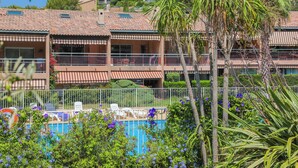 A hotel with a swimming pool, multiple balconies, and lush greenery. - Charming T2 apartment near the sea - Residence with trees and swimming pool (Le Pradet)