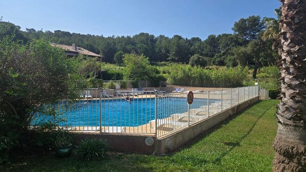 Une piscine rectangulaire entourée d’une clôture métallique, elle-même bordée d’une végétation luxuriante et d’arbres.