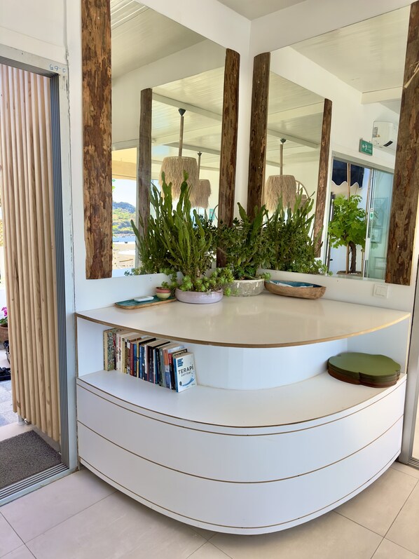 Un moderno mostrador de recepción con diseño curvo, un espejo grande y plantas en macetas.