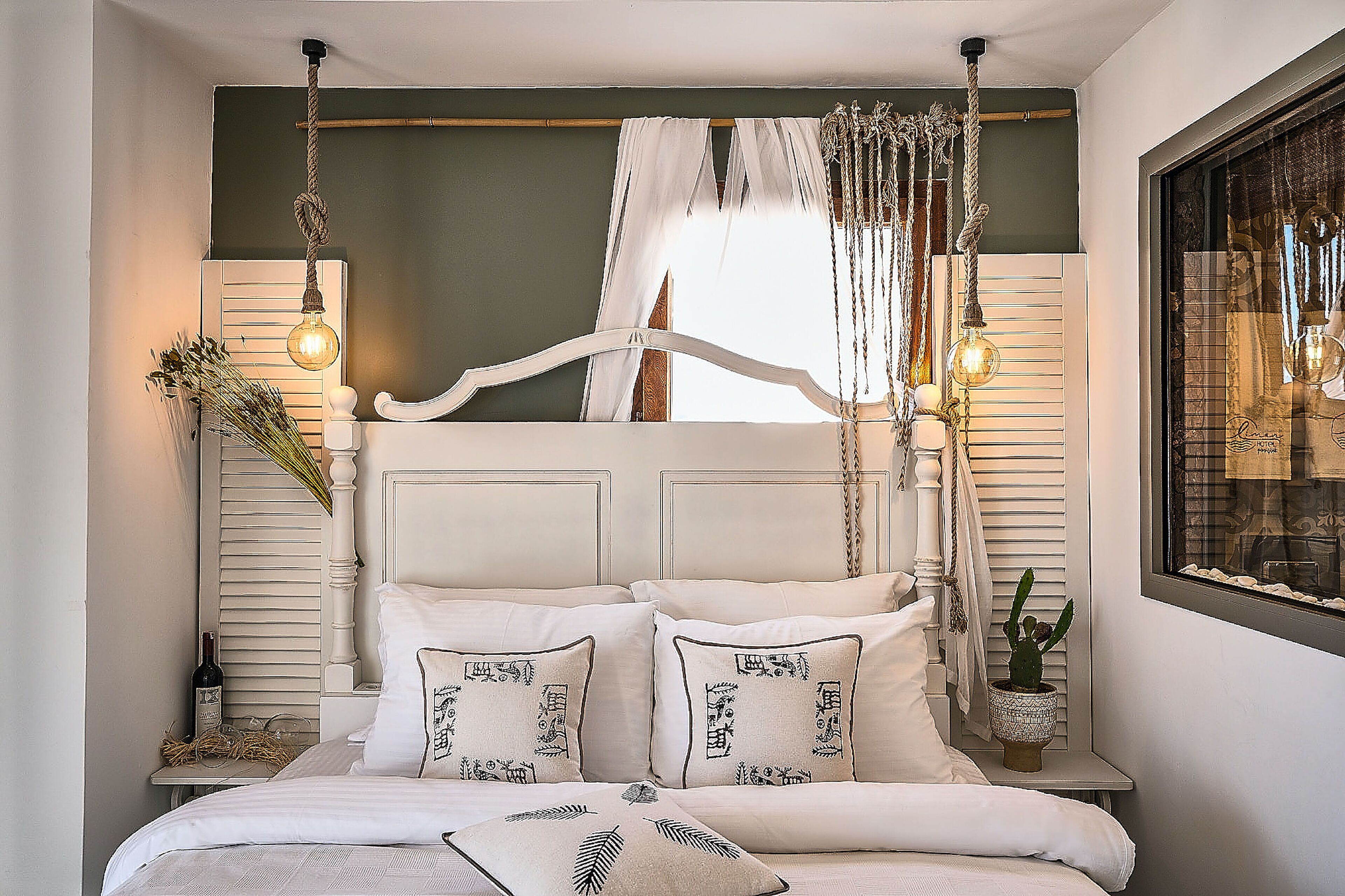 Un dormitorio con cama, mesitas de noche, una ventana con cortinas y una lámpara colgante.