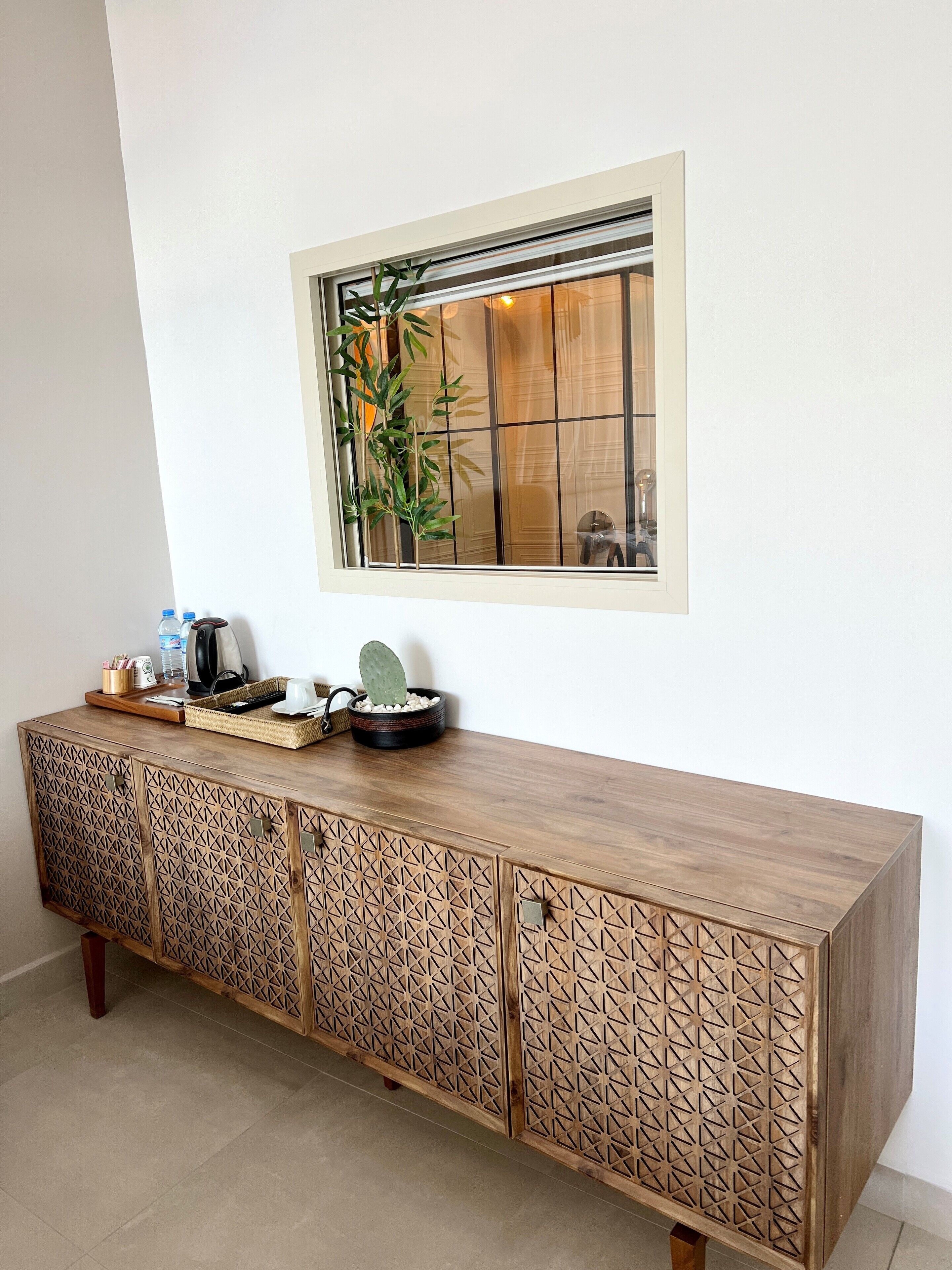 Un mueble de madera con diseños geométricos, una ventana con vistas y una planta en el alféizar.