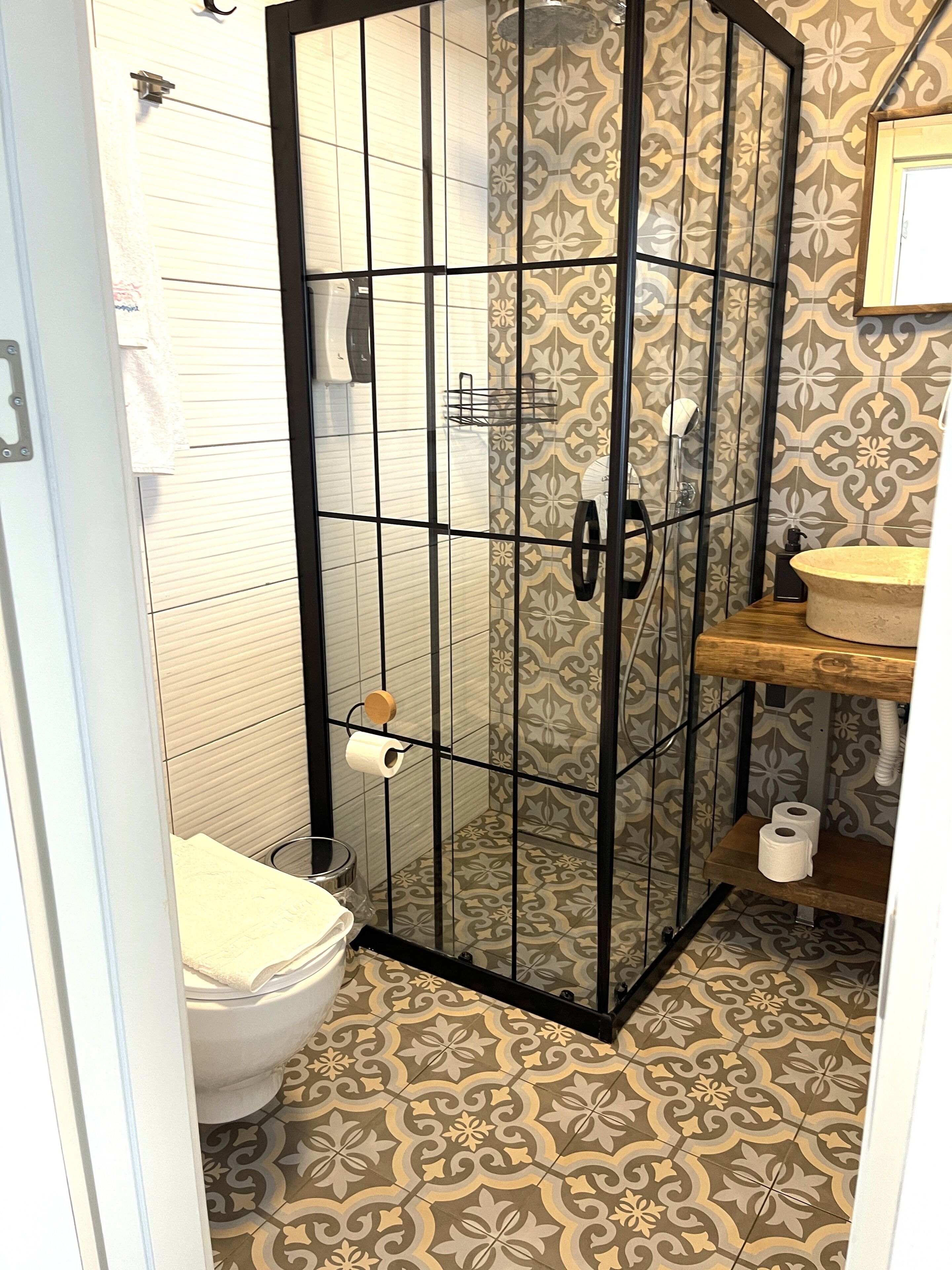 A bathroom with a glass-enclosed shower, a toilet, and a sink with a wooden countertop.