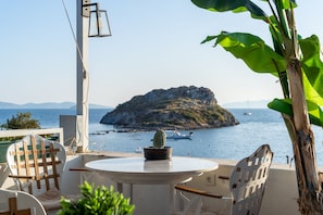 A round table with a potted cactus, white chairs, and a view of a rocky island and boats in the background. - Liman Hotel Gumusluk- Adult Only (Bodrum)