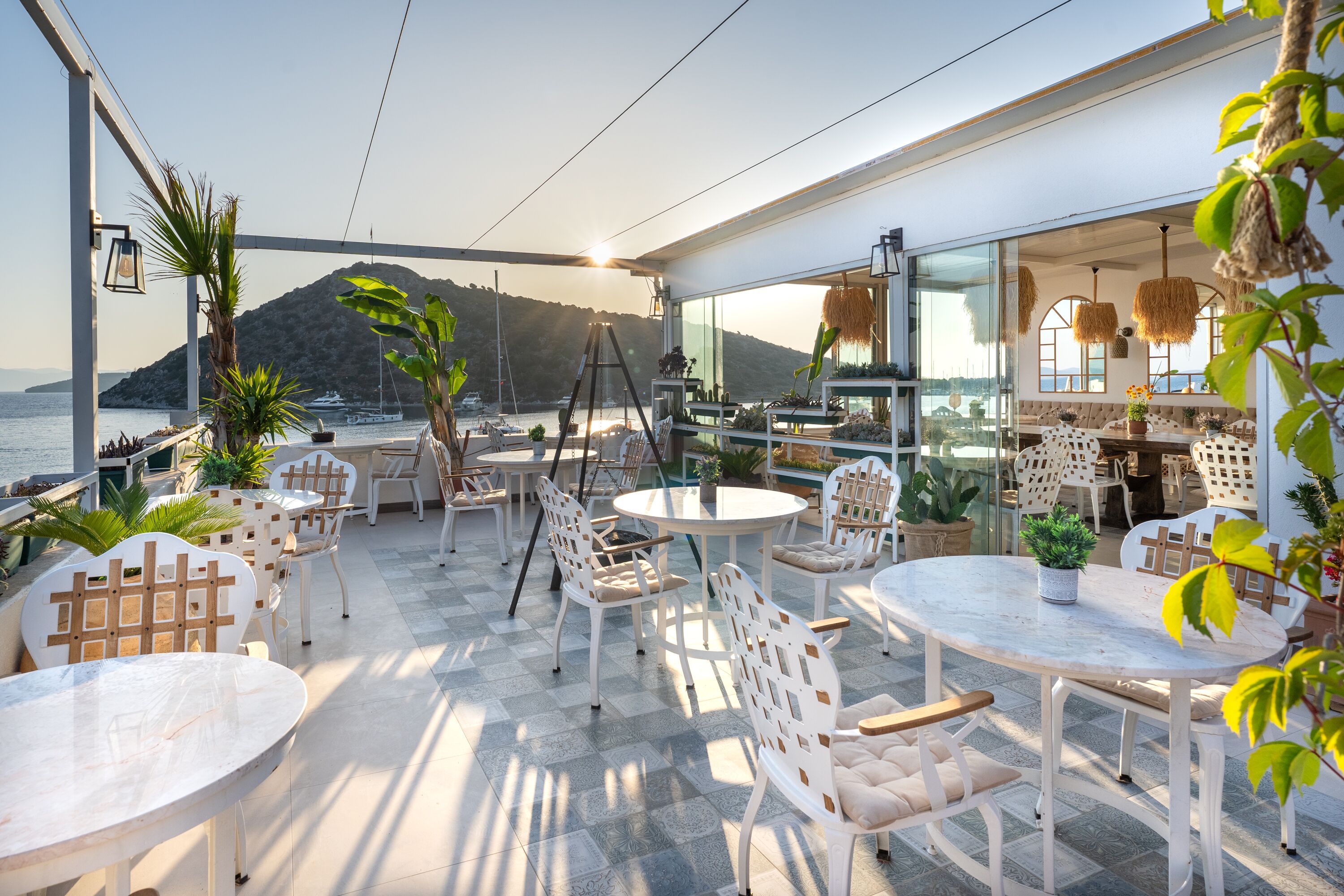 Eine Terrasse im Freien mit weißer Möbel, Blumentöpfen und Blick auf das Meer und die Berge.