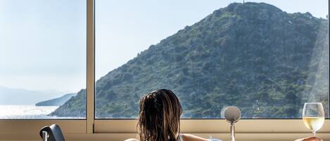 Una persona relajándose en una bañera con vistas a un paisaje montañoso a través de una ventana.