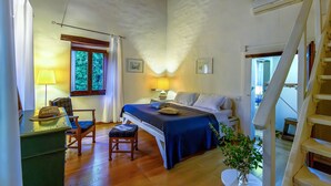 Een gezellige slaapkamer met een bed, nachtkastje, lamp, stoel en uitzicht op het groen door een raam.