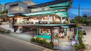 A modern restaurant with a glass facade and outdoor seating area. - Family Pool Home | River Fire City Skyline Views (Balmoral)