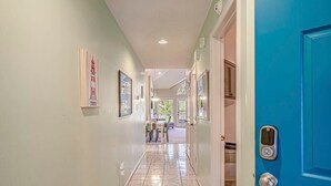 A hallway with a blue door, a dining area with a table and chairs, and framed artwork on the walls.