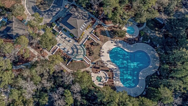 An aerial view of a residential property with a swimming pool, a landscaped garden, and a building with a circular driveway.