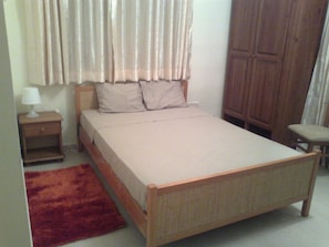 Un dormitorio con una cama individual, una mesita de noche, una lámpara, un armario de madera y una alfombra roja.