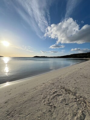 Une plage avec un ciel dégagé, une eau calme et une terre lointaine à l’horizon.