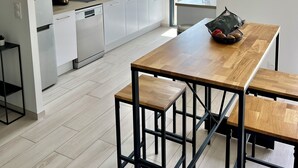 Eine moderne Küche mit weißen Schränken, einem Holztisch und einer hängenden Rattanleuchte.