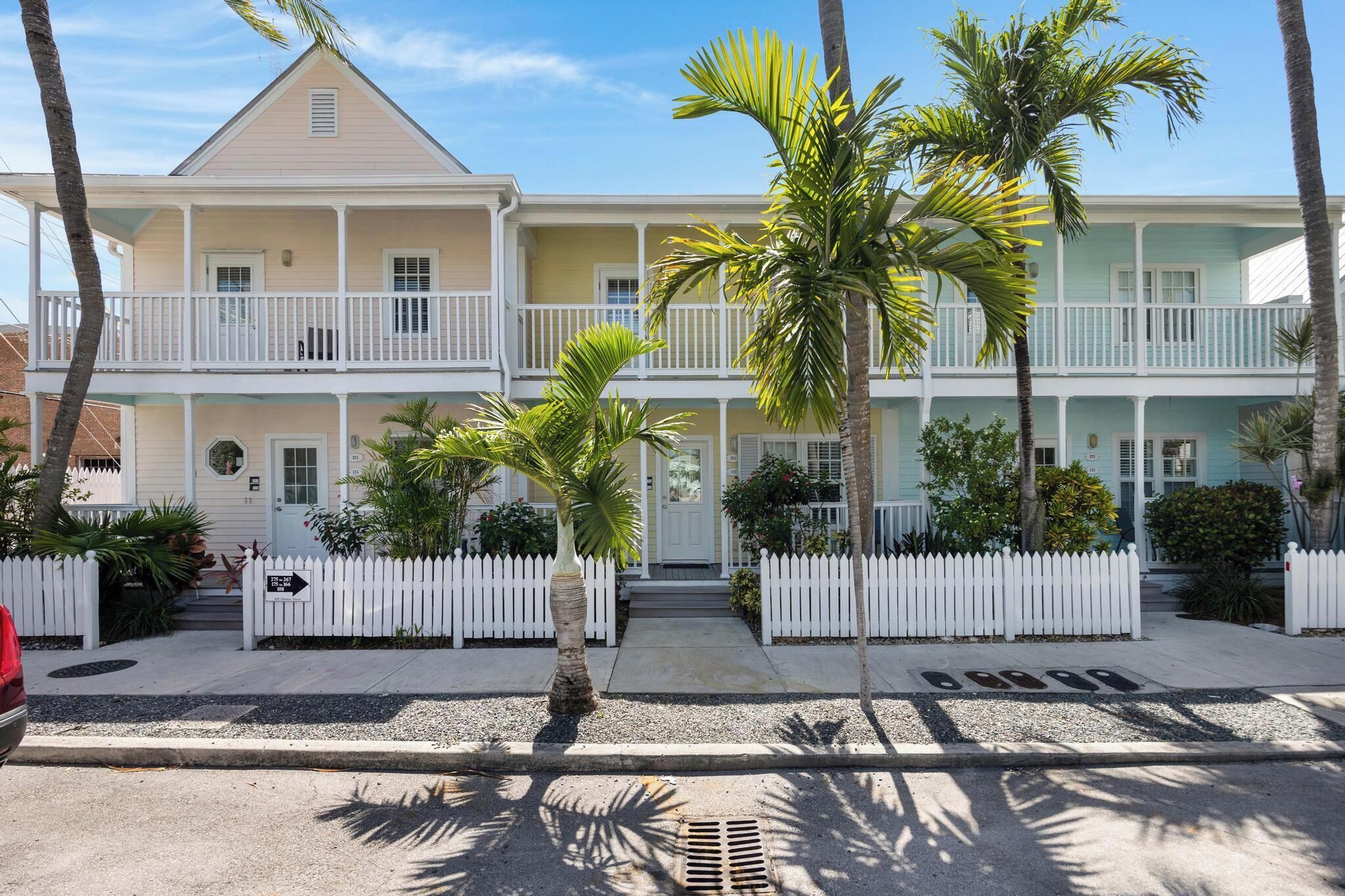 A two-story building with a white picket fence, palm trees, and a clear sky.