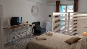 Um quarto com cama, escrivaninha com computador, bicicleta e janela com persianas.