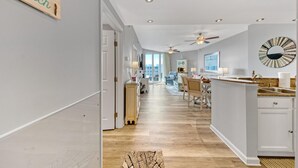 A modern kitchen with a large island, a dining area with a view, and a hallway leading to a bedroom. - Palms of Destin|12th flr Jr Suite-Lagoon Pool|Views (Destin)