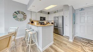 A modern kitchen with white cabinetry, a central island with stools, a stainless steel refrigerator, and a microwave. - Palms of Destin|12th flr Jr Suite-Lagoon Pool|Views (Destin)