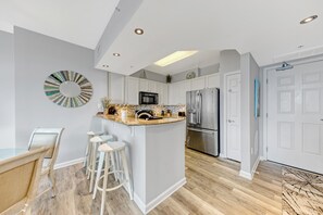 A modern kitchen with white cabinetry, a central island with stools, a stainless steel refrigerator, and a microwave.