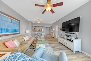 A living room with a sofa, TV, ceiling fan, and a dining area with chairs and a table. - Palms of Destin|12th flr Jr Suite-Lagoon Pool|Views (Destin)