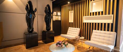 A modern lobby with a white sofa, a round glass table with flowers, and two black sculptures on pedestals.