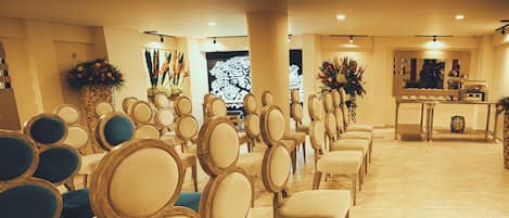 Rows of chairs with wooden frames and cushioned seats, arranged in a banquet hall with a tiled floor and floral centerpieces.