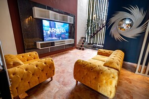 Una sala de estar moderna con un televisor de pantalla plana grande montado en la pared, dos sofás capitonados y un espejo decorativo.