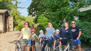 Un grupo de personas en bicicleta en un área de grava con árboles y un edificio al fondo.