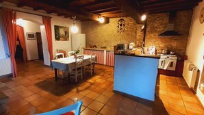 Una cocina rústica con pared de piedra, vigas de madera, un área de comedor con mesa y sillas, y una pequeña isla con un lavamanos.