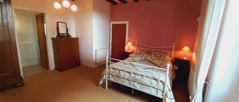 A bedroom with a metal bed frame, two bedside lamps, a wooden dresser, and a door leading to another room.