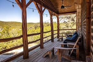 A wooden deck with a bench and a table, overlooking a hilly landscape. - Leakey River Rental, relax in the peaceful hill country or cool off in the river (Leakey)