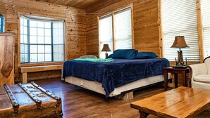 Une chambre à coucher dans une cabane en bois, comprenant un lit, deux lampes de chevet, un banc, une table et une fenêtre avec des stores.