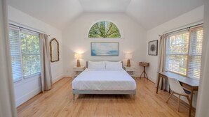 A spacious bedroom with a large bed, two bedside tables, a desk with a chair, and a large window with a view of trees. - Riverfront Retreat 7mil from MD Renaissance Fest! (Riva)