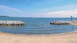 A beach with calm water, a rocky breakwater, and a solitary figure standing on the rocks. - Riverfront Retreat 7mil from MD Renaissance Fest! (Riva)