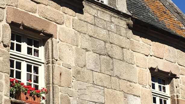 A stone building with two arched windows and flower boxes on the ground floor.