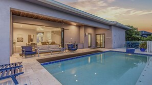 A modern house with a swimming pool, a patio with seating, and a visible interior with a dining area and a bathroom.
