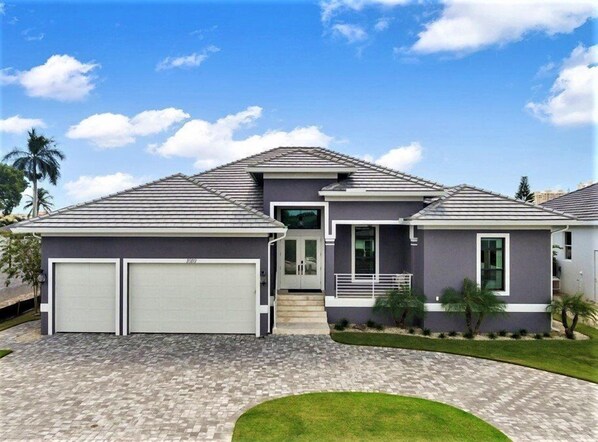 A modern two-story house with a grey roof, two garage doors, and a well-maintained lawn. - Live in Luxury; Walk to the beach, shops and more (Marco Island)