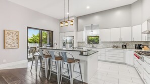 A modern kitchen with a central island, bar stools, stainless steel appliances, and a view to the outdoors.