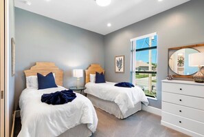 A hotel room with two beds, a dresser, a nightstand, and a window with a view of the outside.