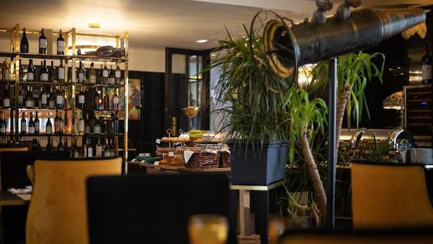 Interior de restaurant amb una botiga de vi, una planta en test i una taula de dinar amb cadires.