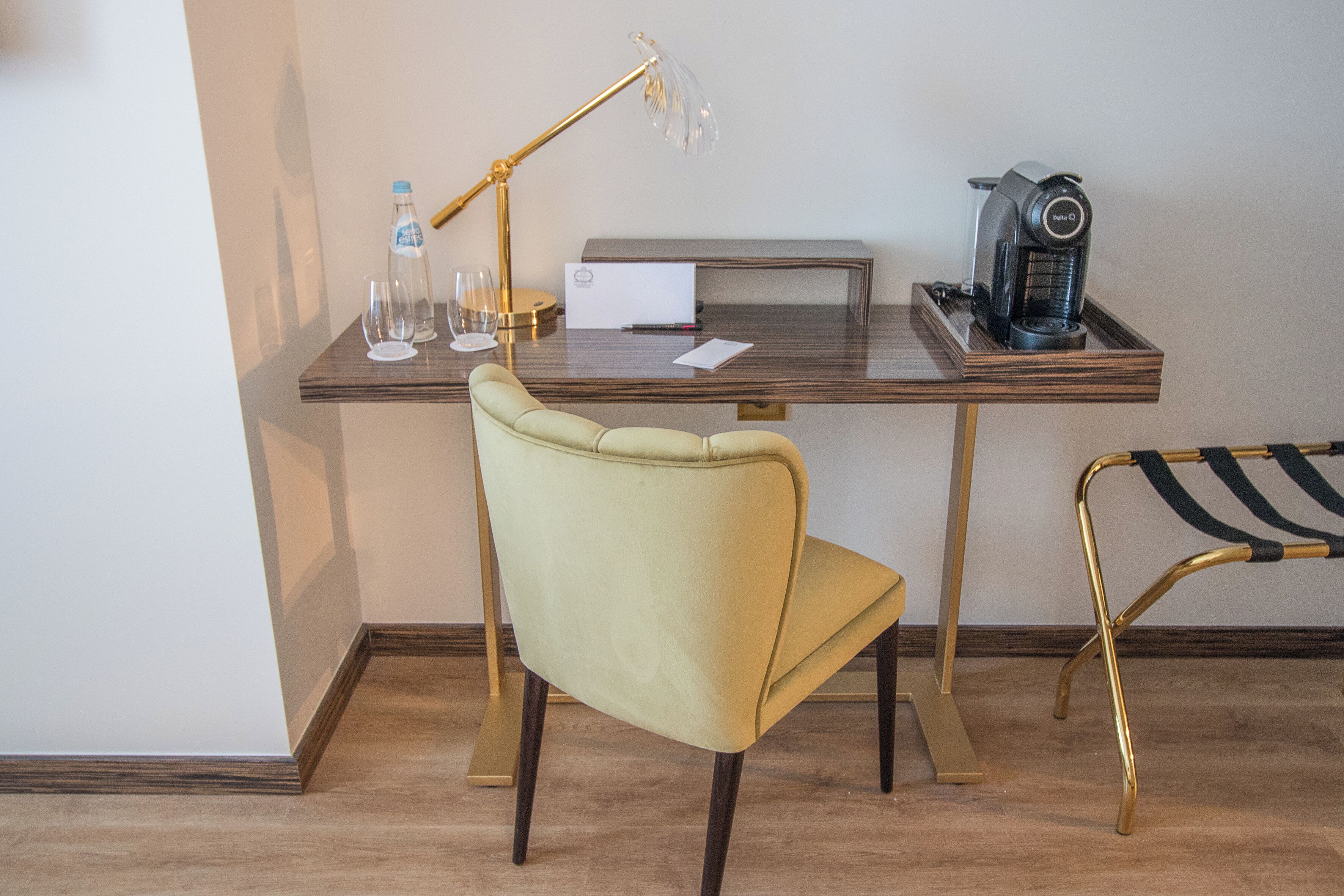 Un espacio de trabajo moderno con escritorio, silla, lámpara, máquina de café y una botella de agua.