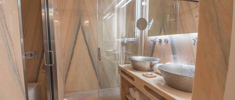 A modern bathroom with a glass-enclosed shower, marble flooring, and a vanity with two large bowls.