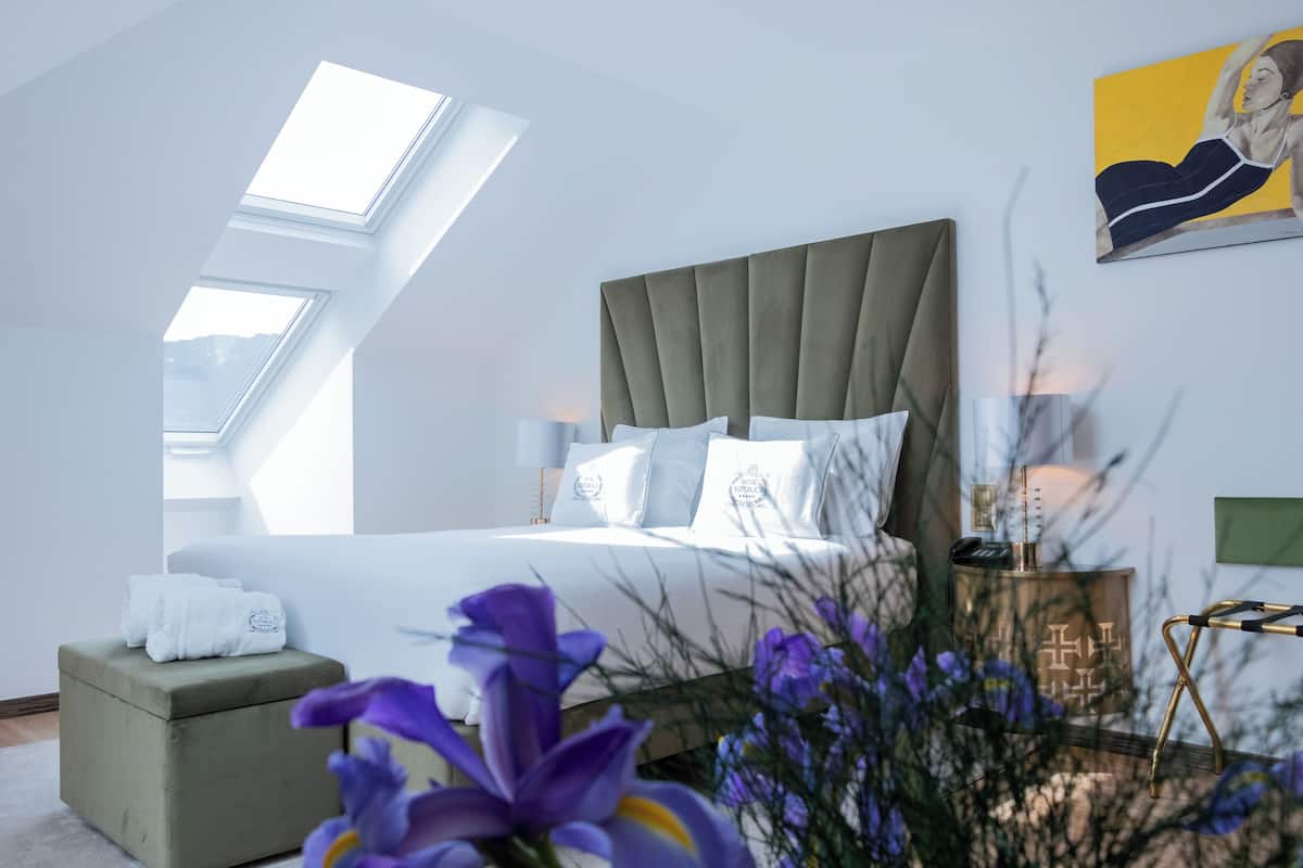 Une chambre moderne avec un grand lit, des fenêtres de toit, un pouf vert et un tableau au mur.