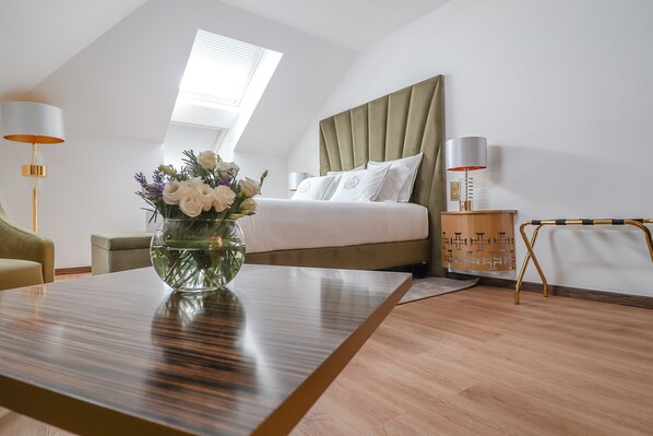 A modern bedroom with a large bed, a bedside table with a lamp, a small table with a vase of flowers, and a view of the sky through a skylight. - Hotel República (Tomar)